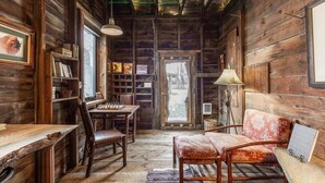 A rustic cabin interior with wooden walls, a chess table, a sofa, a lamp, and a bookshelf. - Grandpa's Cabin Near Yellowstone (Fremont County)