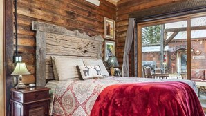 A log cabin-style bedroom with a bed, a nightstand, a lamp, and a window with a view of the outside. - Grandpa's Cabin Near Yellowstone (Fremont County)