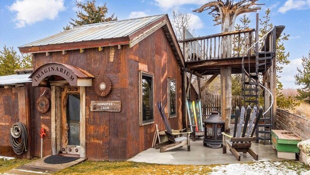 A rustic cabin with a metal roof, a wooden deck, and a staircase leading to a platform. - Grandpa's Cabin Near Yellowstone (Fremont County)