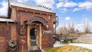 A rustic cabin with a metal roof, a wooden door, and a sign reading 'IMAGINARIUM GRANOPAS CADIN.' - Grandpa's Cabin Near Yellowstone (Fremont County)