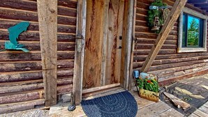 A rustic log cabin with a wooden door, a welcome mat, and a small garden area. - Rustic Trails Near Yellowstone (Fremont County)
