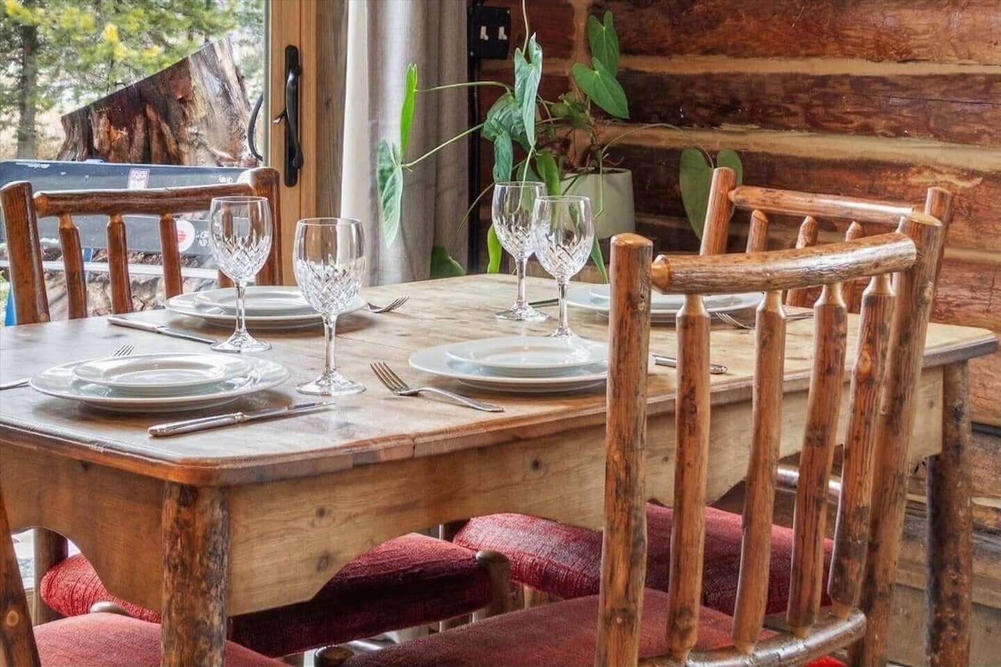 Une table de salle à manger en bois, mise avec des assiettes, des couverts et des verres en cristal, entourée de chaises en bois dotées de coussins rouges.