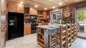 A log cabin kitchen with wooden cabinets, a black refrigerator, a microwave, a stove, and a large island with bar stools. - Rustic Trails Near Yellowstone (Fremont County)