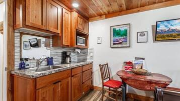 Une cuisine avec des meubles en bois, un plan de travail en granit, une machine à café et un coin repas comprenant une table et des chaises en bois.