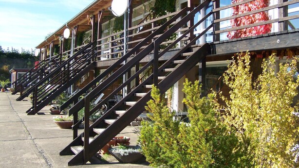 A row of wooden buildings with external staircases, potted plants, and hanging lights. - Rollstuhlgerechte Ferienwohnung im Ferienpark (Dabel)