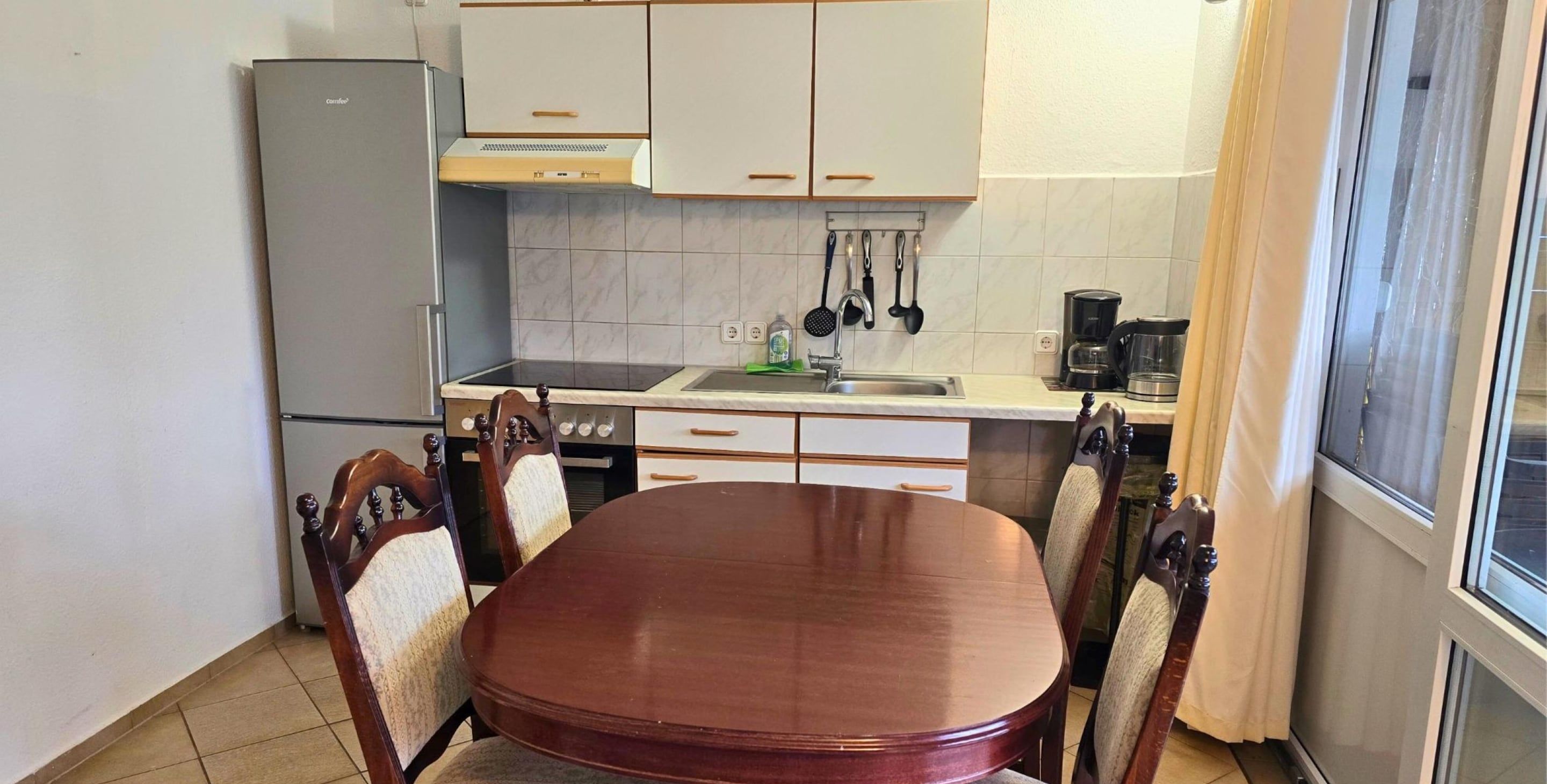 Una cucina compatta con un tavolo da pranzo, sedie, un frigorifero, un fornello e una macchina da caffè.