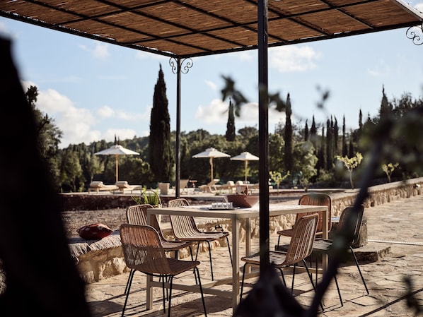 Un patio al aire libre con sillas y mesas de mimbre, sombrillas y vistas a árboles y colinas.