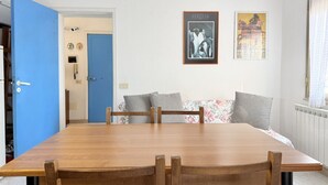Un comedor con una mesa y sillas de madera, una puerta azul y dos cuadros en la pared.
