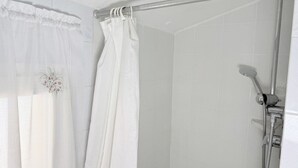 Una ducha con cabezal de ducha manual, barra de cortina metálica y cortina de ducha blanca con bordados florales.