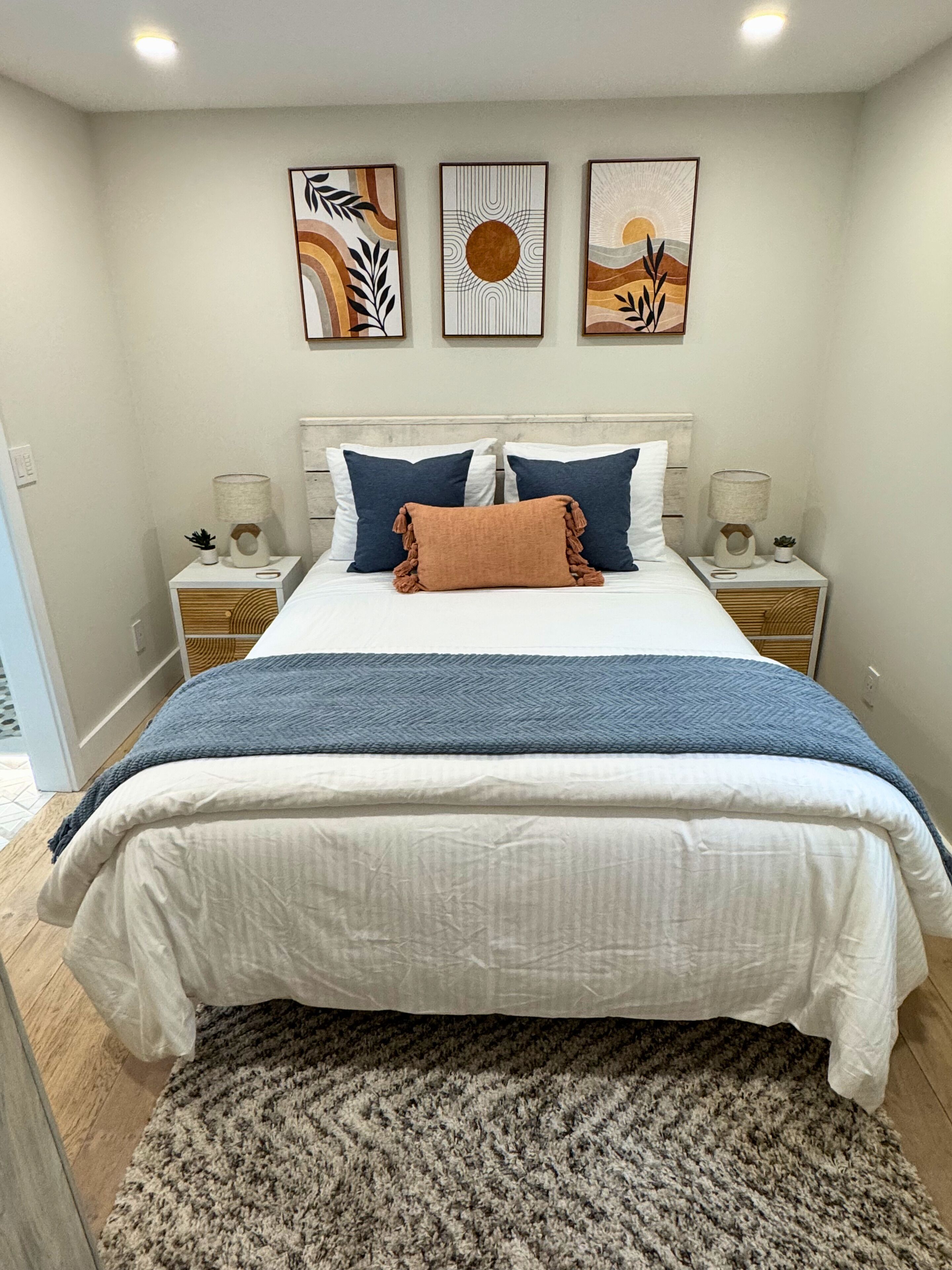 Een slaapkamer met een bed, nachtkastjes, een vloerkleed en drie decoratieve wandobjecten.