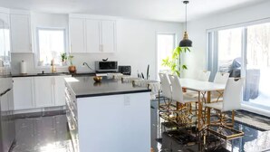 Une cuisine moderne avec des meubles blancs, un îlot central et un coin repas comprenant une table et des chaises blanches.