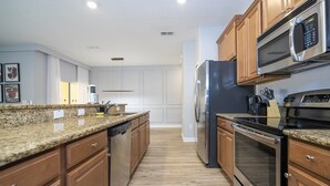 Una cocina moderna con encimeras de granito, electrodomésticos de acero inoxidable, armarios de madera y lavavajillas.