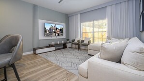 Una sala de estar moderna con una televisión de pantalla plana, un ventilador de techo, un sofá, una butaca y una ventana con cortinas.