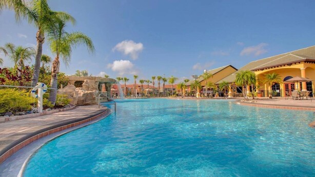 Una piscina con tobogán de agua, palmeras y edificios de un complejo turístico.