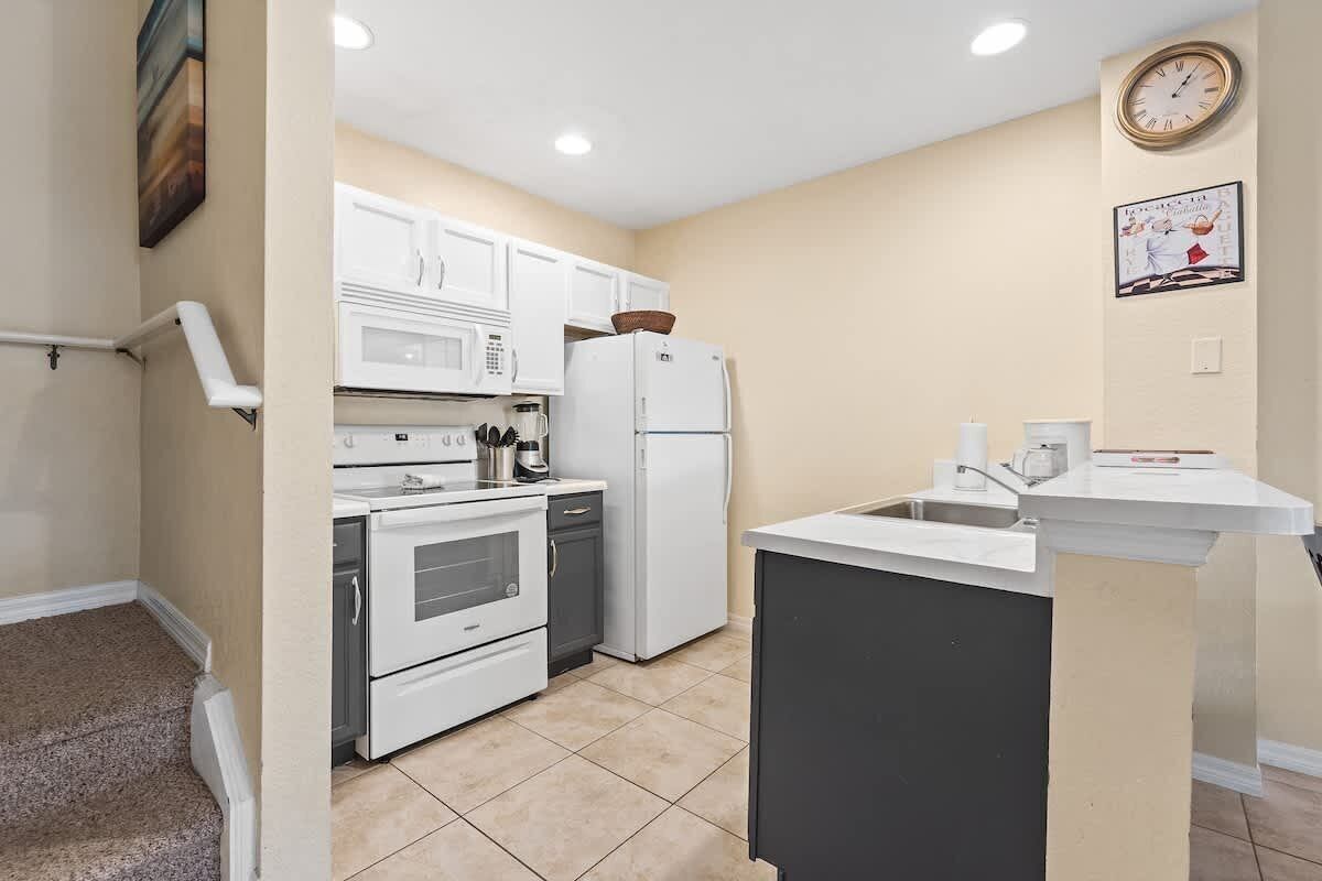Una cocina funcional con electrodomésticos blancos, una pequeña isla y un reloj en la pared.
