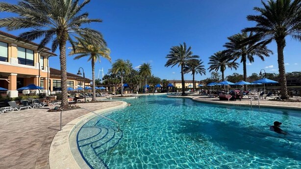 A swimming pool with clear blue water, surrounded by palm trees and lounge chairs. - 3BR Townhome at Regal Oaks Near Disney (Kissimmee)