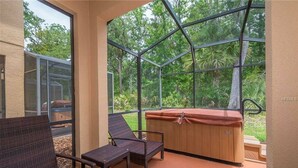 A covered outdoor seating area with wicker furniture, a hot tub, and a view of a lush garden. - 3BR Townhome at Regal Oaks Near Disney (Kissimmee)