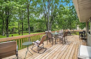 Una terraza de madera con mobiliario exterior, una parrilla y vistas a zona boscosa.