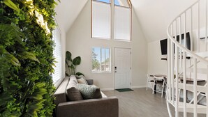 A room with a high ceiling, a built-in plant wall, a gray sofa, a white door, and a white spiral staircase.