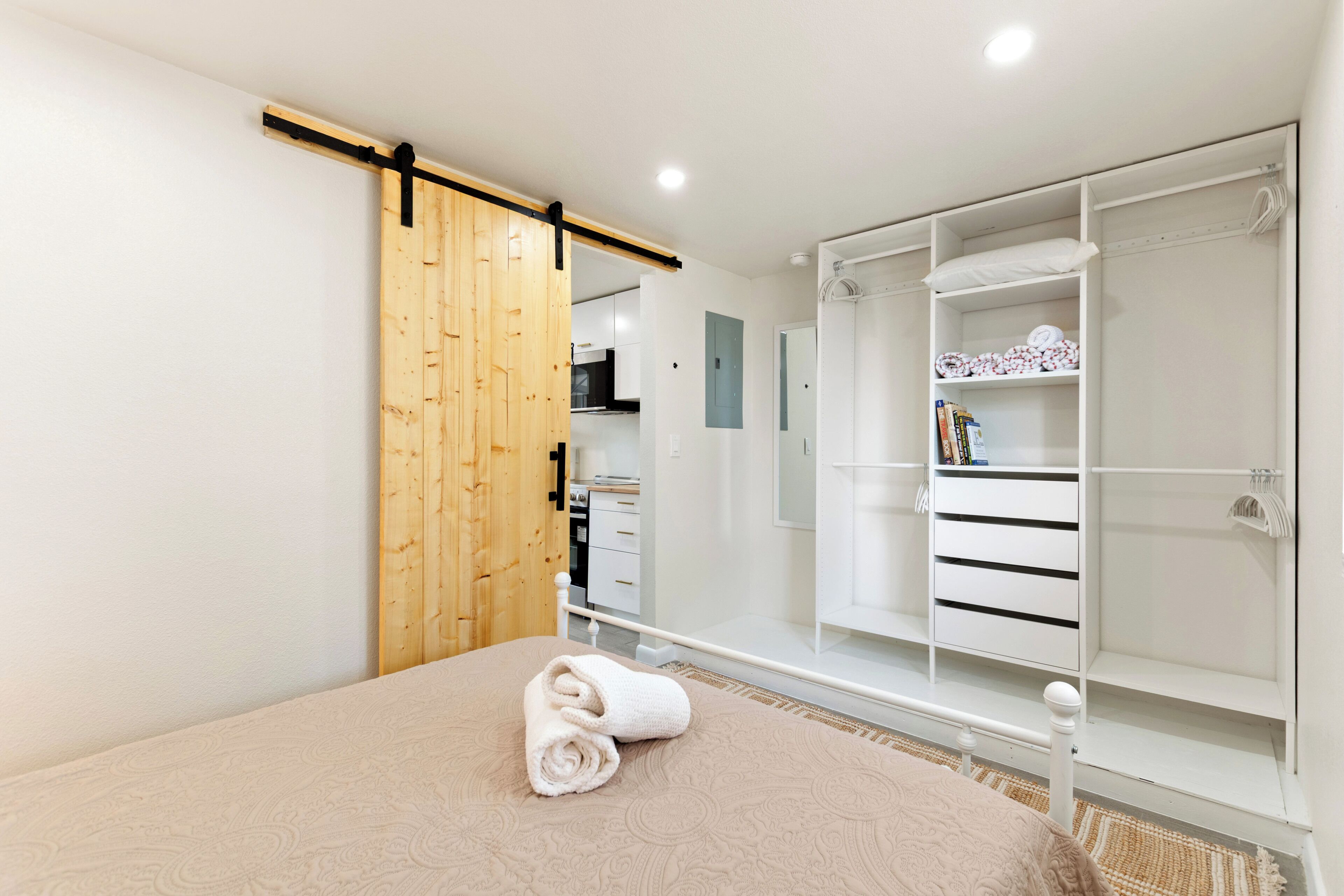 Une chambre à coucher avec un lit, une porte coulissante en bois, une armoire blanche et une salle de bain visible à travers une porte ouverte.