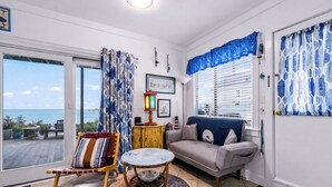 A living room with a sofa, a chair, a small table, a lamp, and a view of the sea. - *NEW* Beachfront Condo - Prime Commercial St Location (Provincetown)