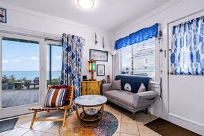 Sala de estar com sofá, poltrona, mesinha, luminária e vista para o mar.