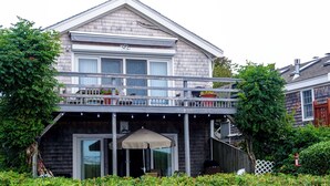 A two-story house with a balcony, a covered patio, and a garden with flowers. - *NEW* Beachfront Condo - Prime Commercial St Location (Provincetown)
