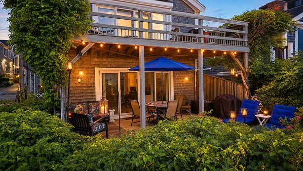 A wooden deck with outdoor seating, string lights, and a covered patio area. - *NEW* Beachfront Condo - Prime Commercial St Location (Provincetown)