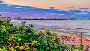 Vista costeira com um cais, uma praia e uma rede de proteção vermelha.