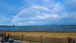 A beach with a wooden fence, a boat-filled harbor, and a rainbow. - *NEW* Beachfront Condo - Prime Commercial St Location (Provincetown)
