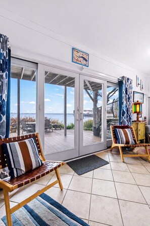 Quarto com uma grande porta de correr de vidro que dá para um deck externo com vista para a água. Há duas cadeiras de madeira com almofadas listradas.