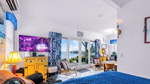 A hotel room with a bed, a TV, a desk, a chair, a lamp, and a view of the sea. - *NEW* Beachfront Condo - Prime Commercial St Location (Provincetown)