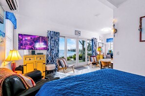 Un cuarto de hotel con una cama, televisión, escritorio, silla, lámpara y vista al mar.