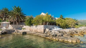 Une propriété située en bord de mer, dotée d’une piscine, de chaises longues et d’un mur en pierre.