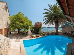 A pool area with a view of the sea, a stone building, and a palm tree. - Luxury Seafront Villa Mare Orebic With Pool (Orebic)