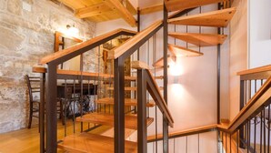 Un escalier en bois avec des rampes en métal, un mur en pierre et un coin repas avec des chaises et une table.
