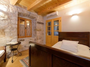 A bedroom with a stone wall, wooden ceiling, a bed, a small table, and a door with glass panels. - Luxury Seafront Villa Mare Orebic With Pool (Orebic)