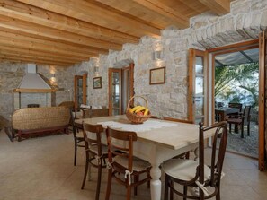 A stone-walled dining area with a wooden ceiling, a table with chairs, and a wicker sofa. - Luxury Seafront Villa Mare Orebic With Pool (Orebic)