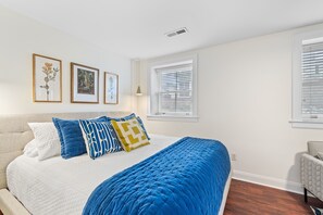 Quarto com cama, janela com persianas e obra de arte pendurada na parede.