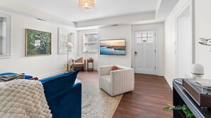 Ein modernes Wohnzimmer mit einem blauen Sofa, einem weißen Sessel, einem Teppich und einem an der Wand befestigten Fernseher.