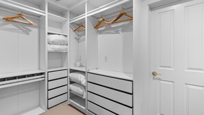 Ein begehbarer Kleiderschrank mit weißen Regalen, hölzernen Kleiderbügeln und einer weißen Tür.