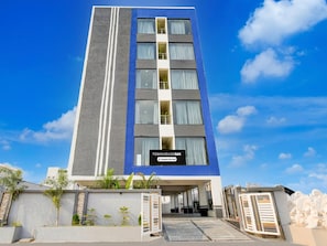A modern multi-story hotel with a prominent entrance, a sign indicating it is a company-serviced property, and a clear blue sky in the background. - Deluxe Saka Arcade (Hyderabad)