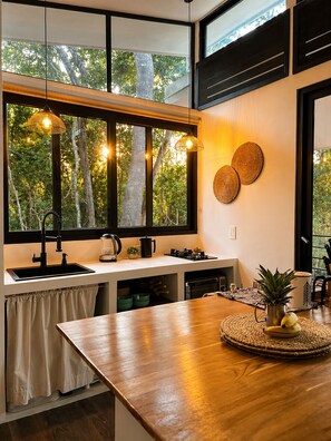 A modern kitchen with large windows, a wooden countertop, and hanging pendant lights. - Jungle Home Escape private hot tub near beaches (Playa Matapalo)