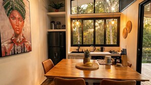 Ein moderner Essbereich mit einem Holztisch, zwei Stühlen und einem großen Fenster mit Blick auf Bäume.