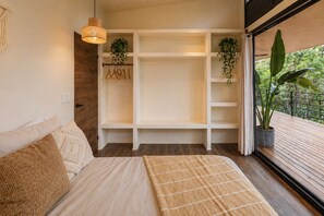 A bedroom with a bed, a hanging light fixture, a built-in shelving unit, and a view of greenery outside. - Jungle Home Escape private hot tub near beaches (Playa Matapalo)