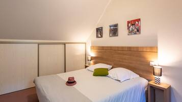 Une chambre à coucher avec un lit simple, deux lampes de chevet, une tête de lit en bois et trois tableaux accrochés au mur.