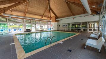 Una piscina interior con agua cristalina, rodeada de suelo de baldosas y sillones blancos.