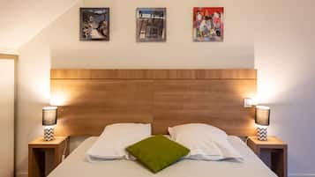 Une chambre à coucher avec une tête de lit en bois, deux lampes de chevet, un lit avec du linge de lit blanc et un oreiller vert, et trois tableaux encadrés accrochés au mur.