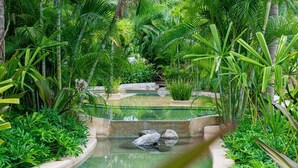 Un jardín interior tranquilo con una fuente central, rodeado de abundante vegetación y senderos de piedra.