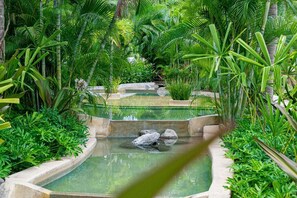 Un jardin intérieur paisible, avec une fontaine centrale, entouré d’une végétation luxuriante et de sentiers en pierre.